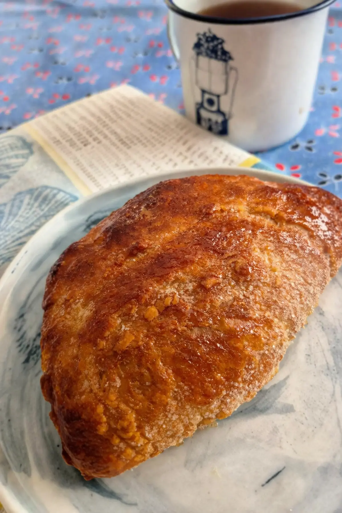 Freshly baked sugar-coated pastry served on a plate with a cup in the background.
