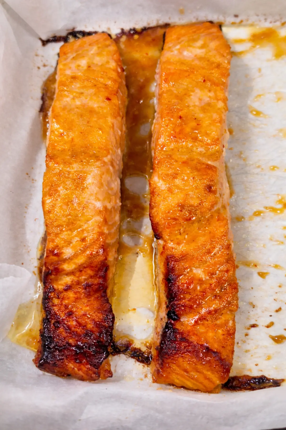 Baked salmon fillets with a caramelised glaze and slightly crisp edges on parchment paper.