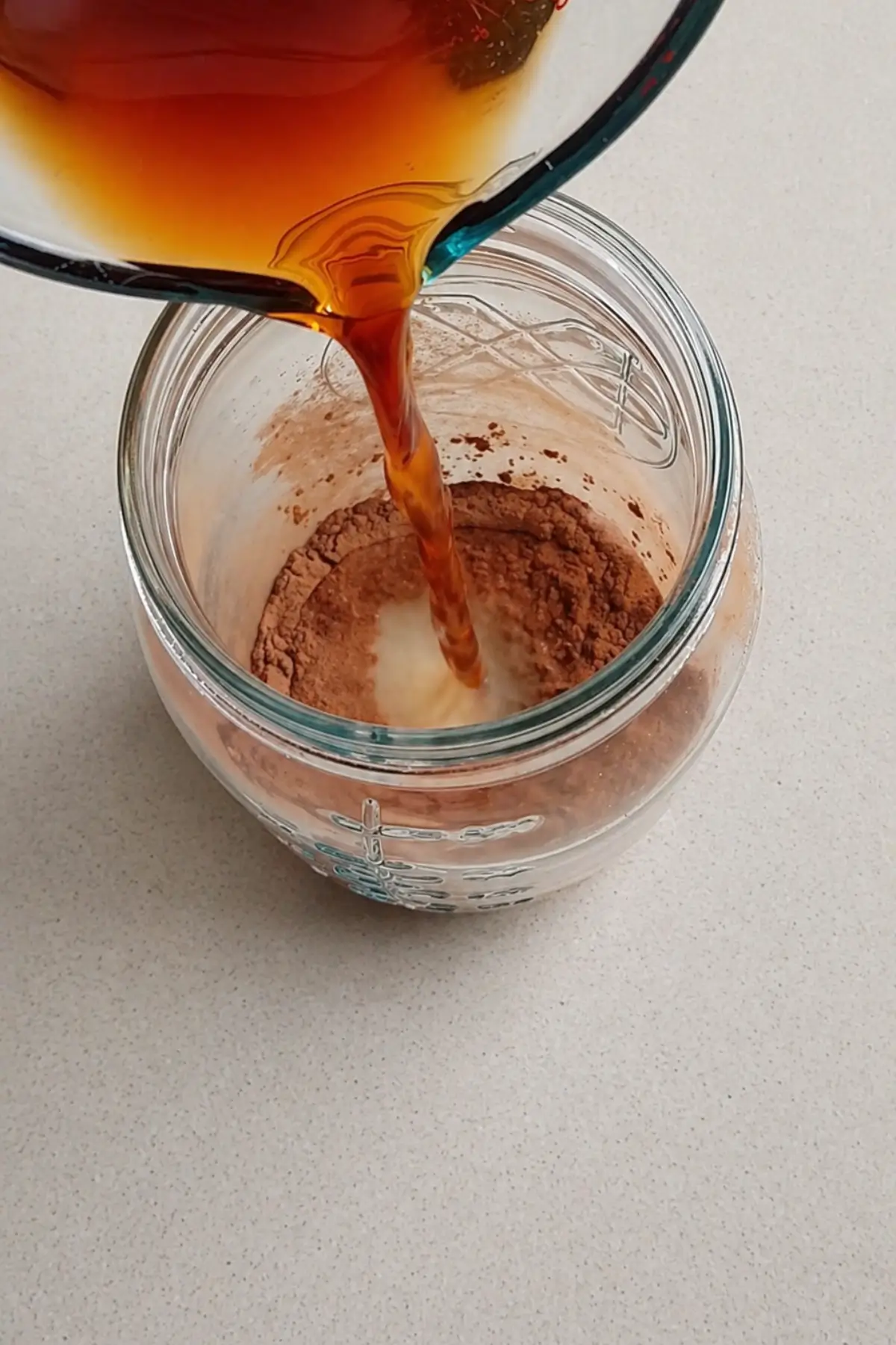 Hot brewed tea being poured over ground spices in a jar.