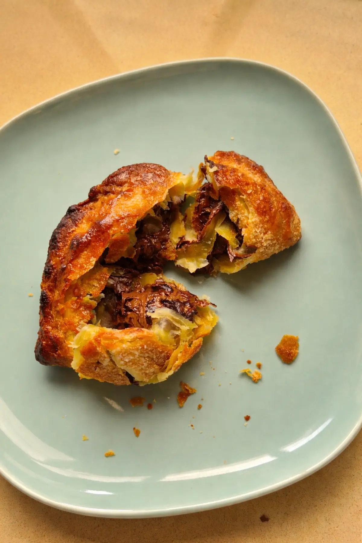 Cut pastry revealing layered interior and melted filling on a plate.