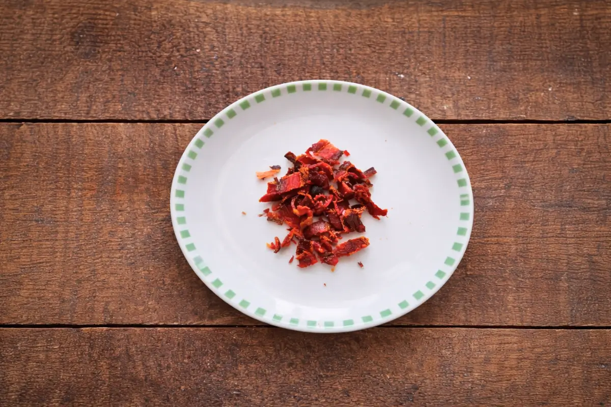 Cooked bacon crumbled into small crisp pieces on a plate.