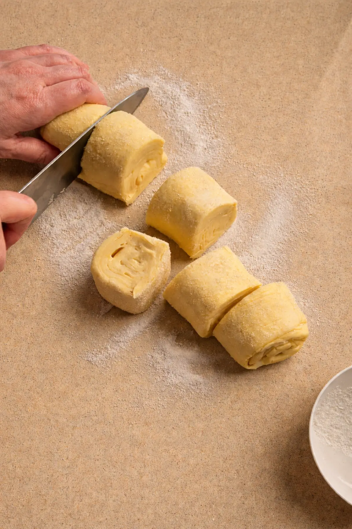 Slicing a sugar-coated puff pastry log into thick pieces on a lightly floured surface.