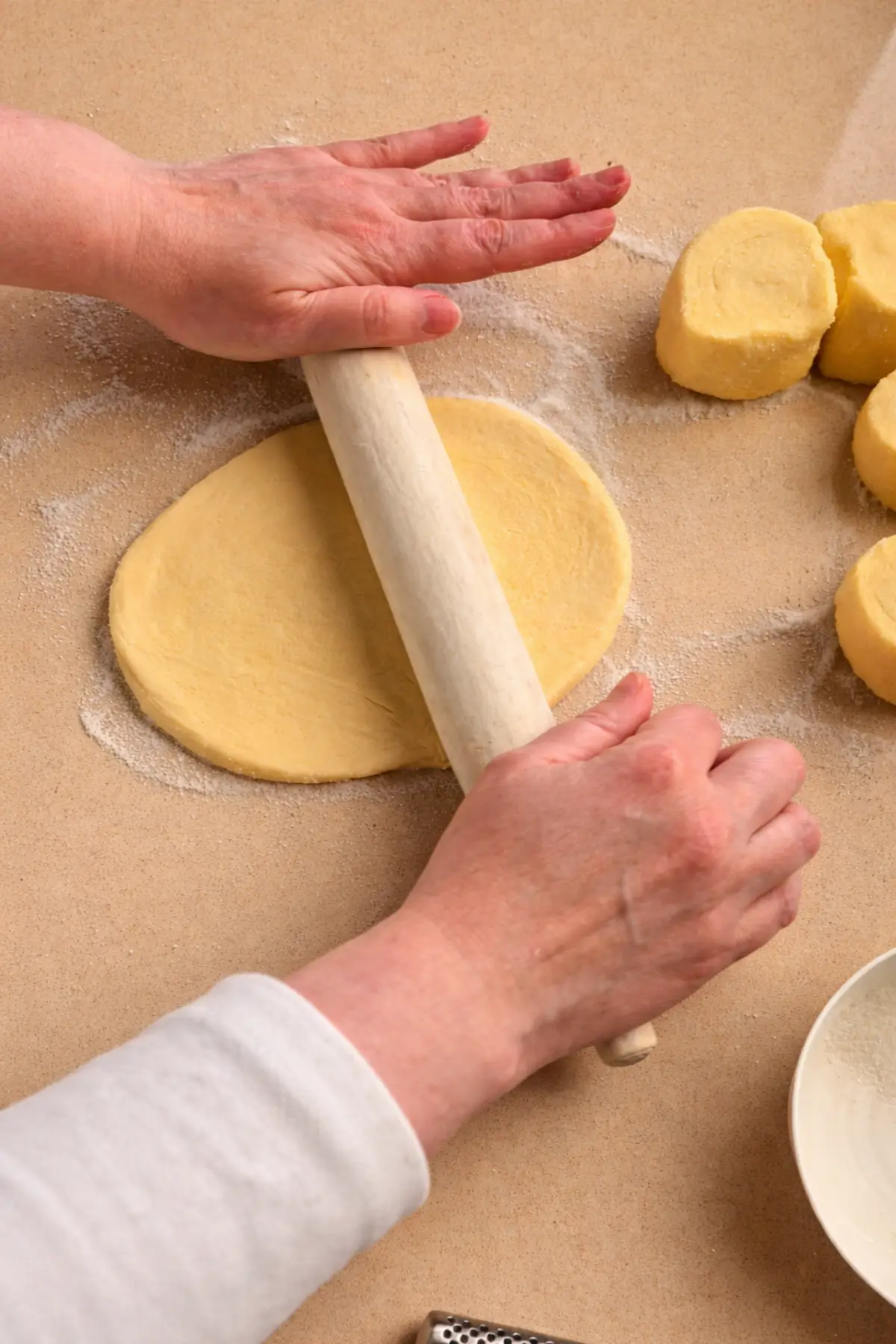 Rolling a sugar-coated pastry slice into an oval with a rolling pin.