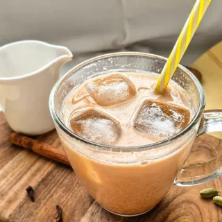 Homemade chai latte with ice served in a glass on a wooden board with spices.