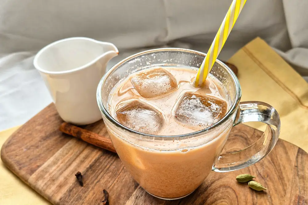 Homemade chai latte with ice served in a glass on a wooden board with spices.
