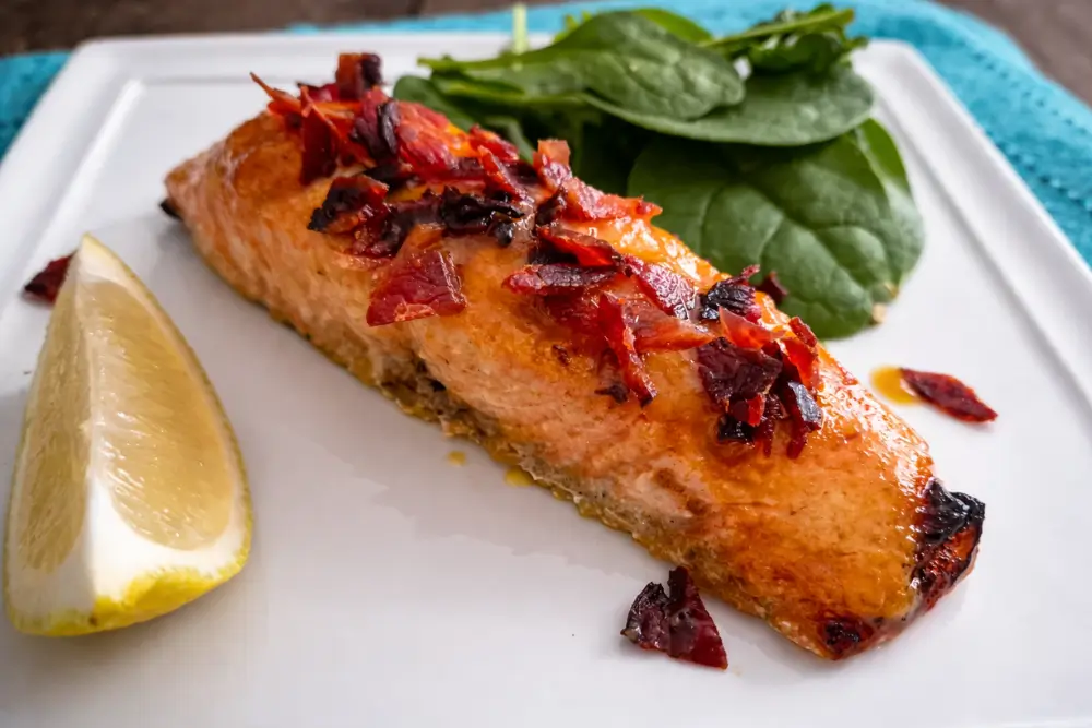 Maple and Sriracha Salmon with Bacon Crumbs served with a lemon wedge and fresh spinach.