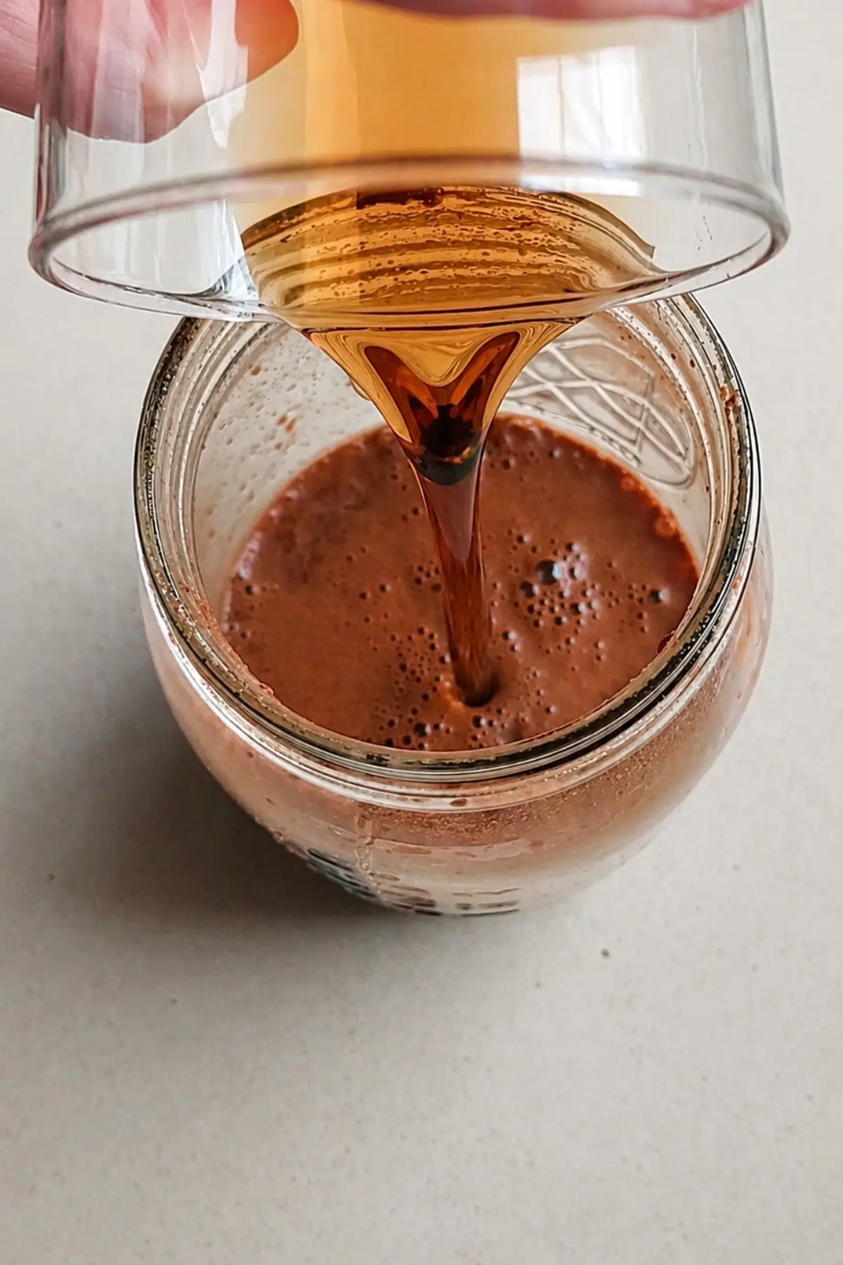 Maple syrup being poured into a jar with spiced tea mixture for chai tea concentrate.