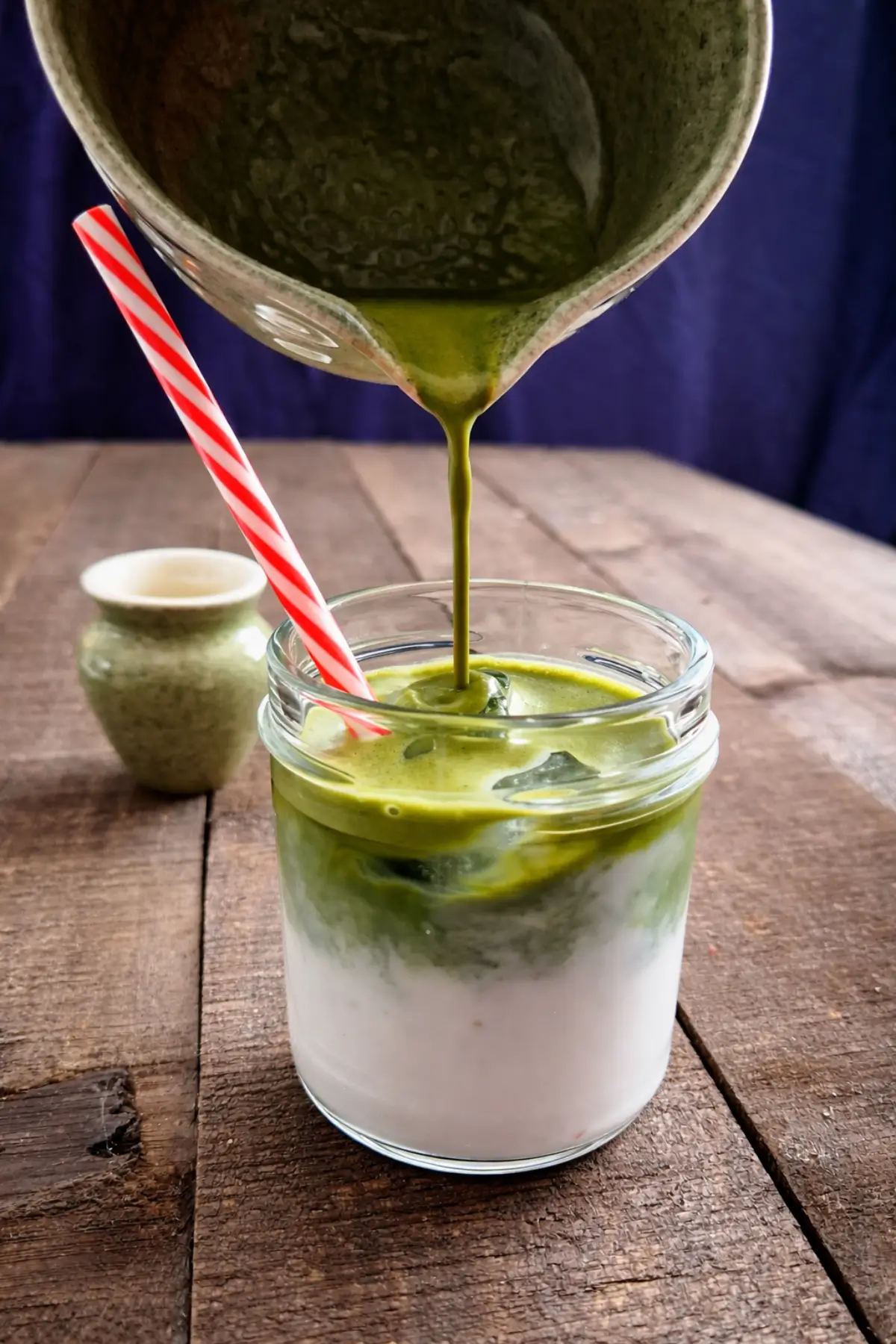 Freshly whisked matcha being poured over ice and milk in a glass.