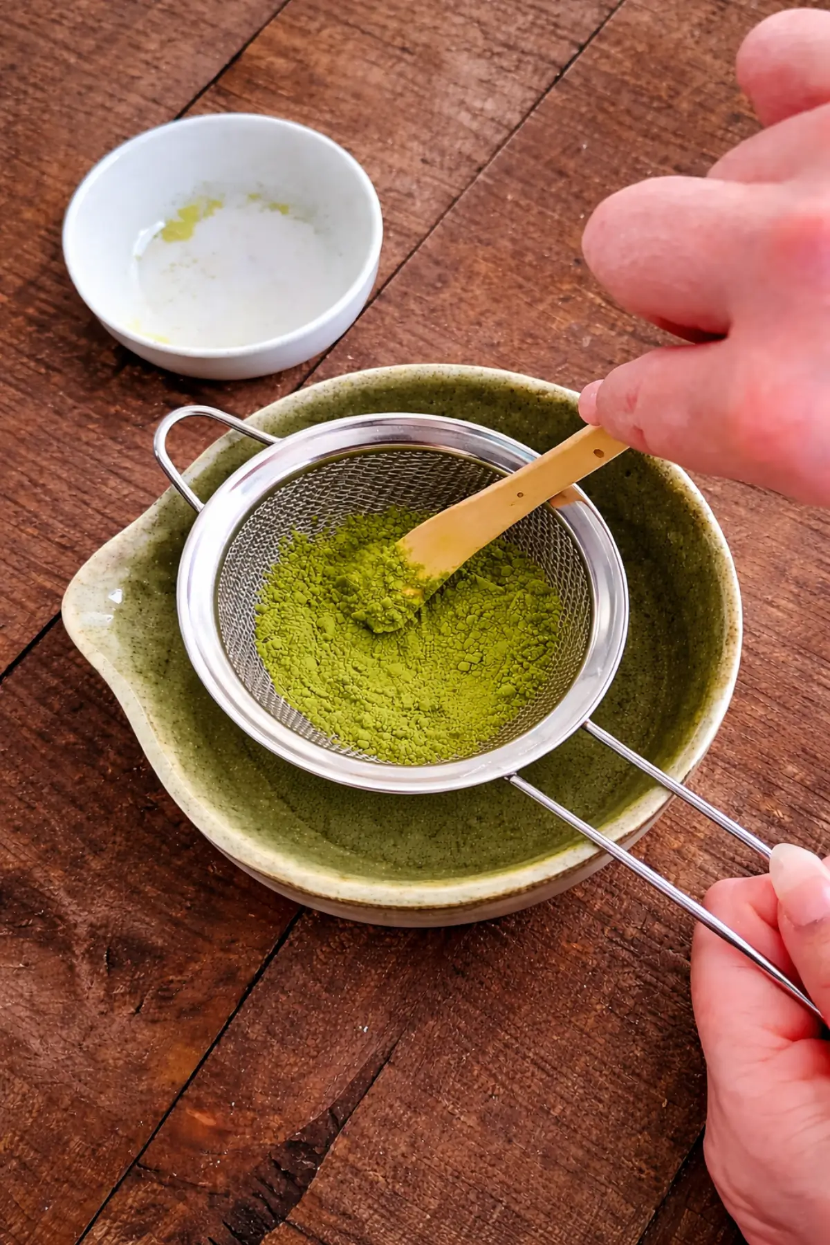 Fine green tea powder being pressed through a sieve into a bowl.