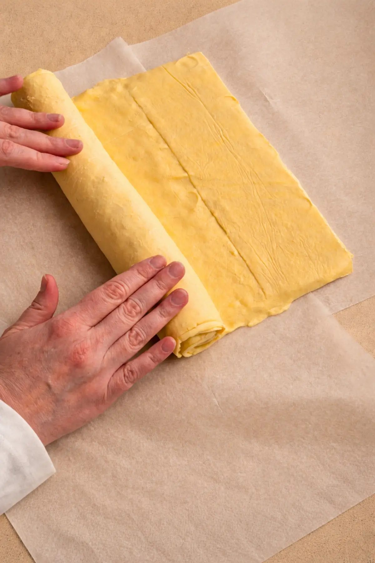 Rolling stacked puff pastry sheets into a tight log on baking paper.