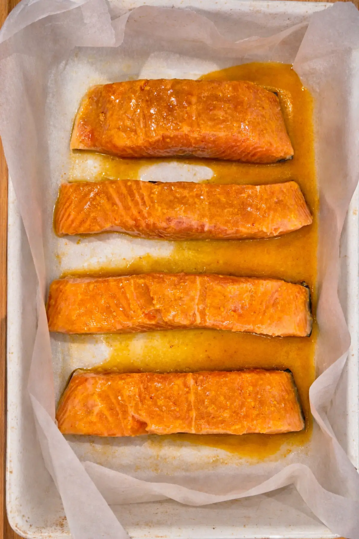 Salmon fillets coated in maple and sriracha glaze arranged on a lined baking tray.