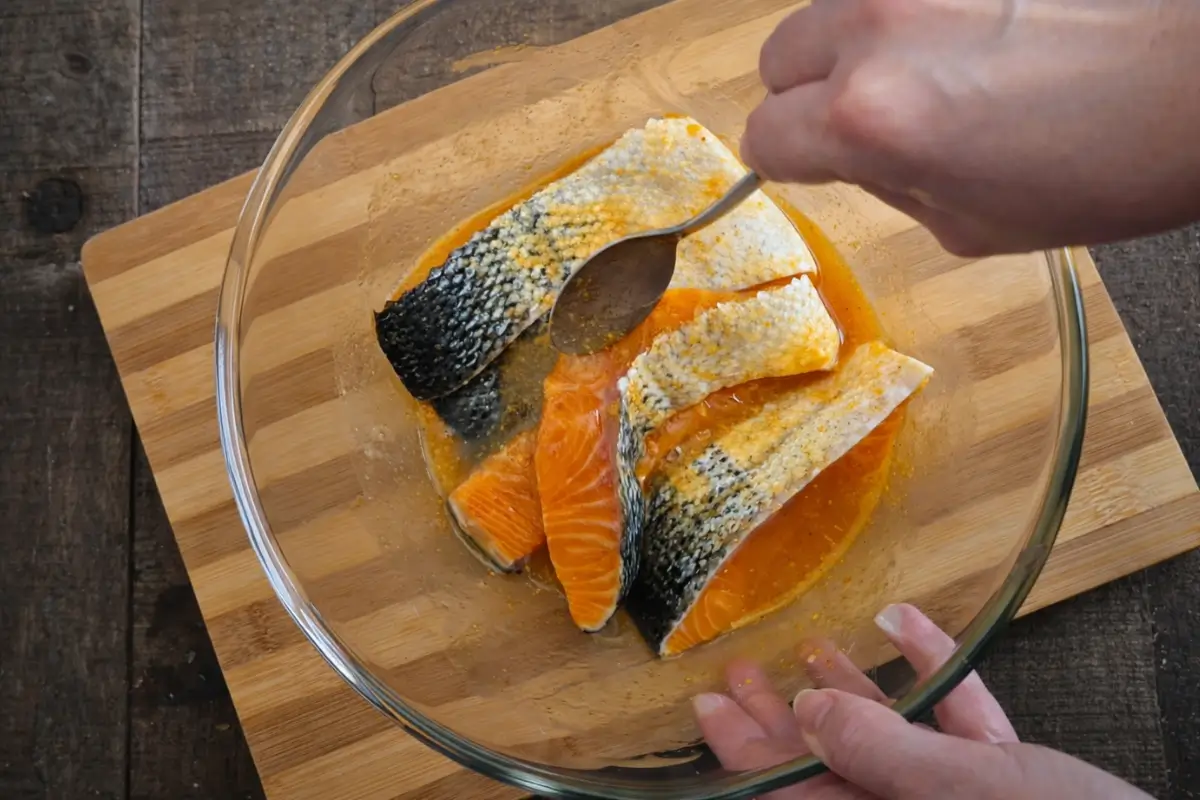 Salmon pieces coated in a maple and sriracha marinade in a glass bowl.