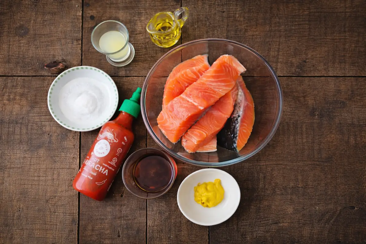 Raw salmon fillets with measured ingredients arranged on a wooden surface.