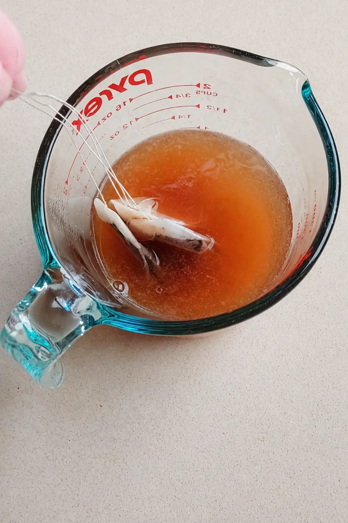 Tea bags steeping in hot water inside a glass measuring jug.