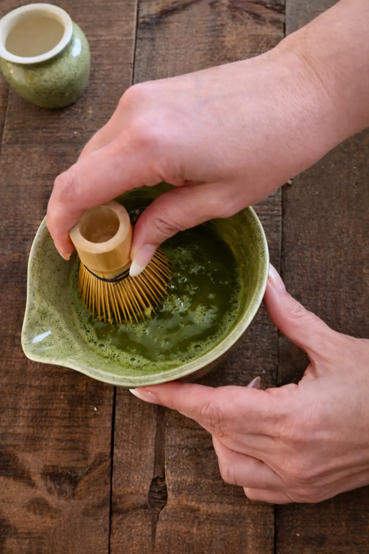 Bamboo whisk mixing matcha green tea powder with water in a bowl.