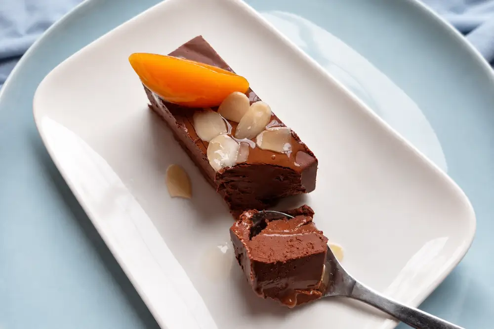 Spoon lifting a rich slice of chilled chocolate and peach dessert.