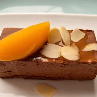 Slice of peach chocolate dessert topped with almond flakes and a peach slice.