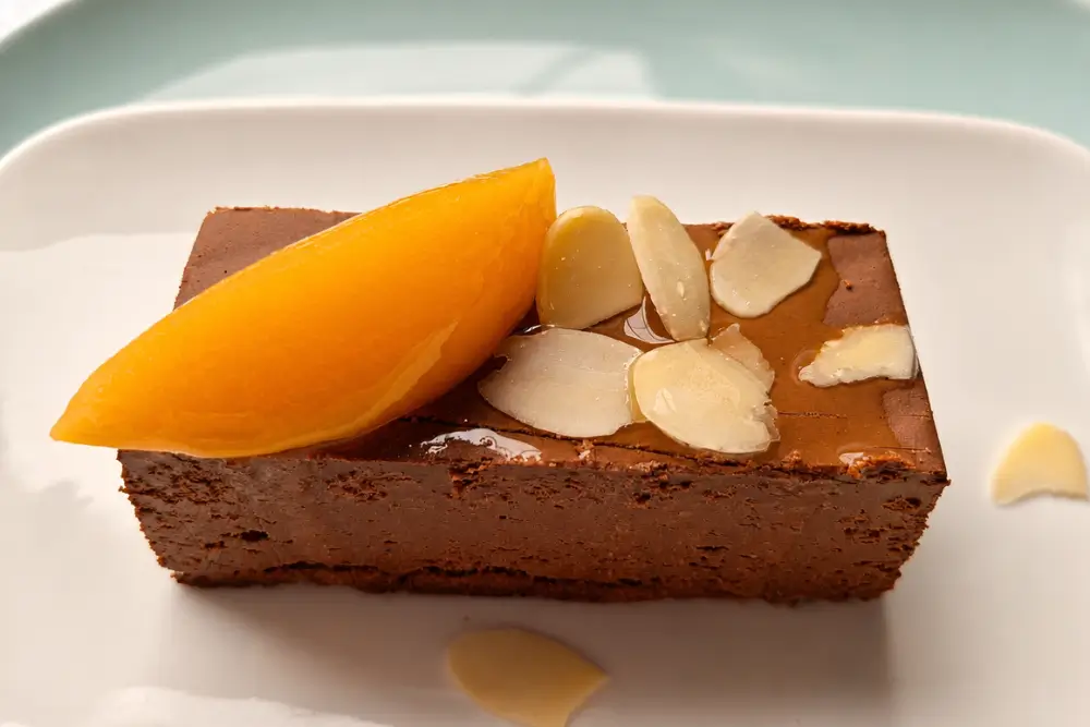 Slice of peach chocolate dessert topped with almond flakes and a peach slice.