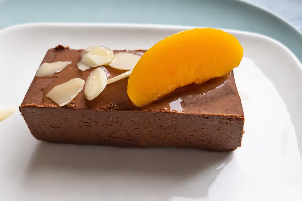 Chocolate dessert slice topped with peach and almond flakes.
