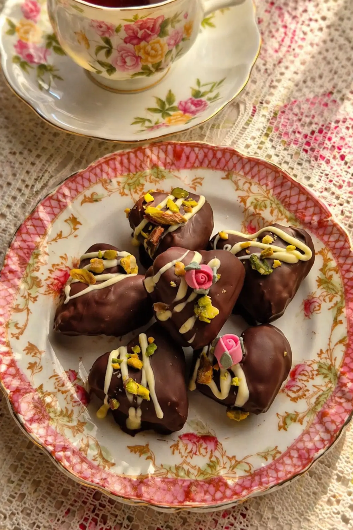 Pistachio chocolate dates decorated with white chocolate drizzle and sugar flowers on a floral plate.