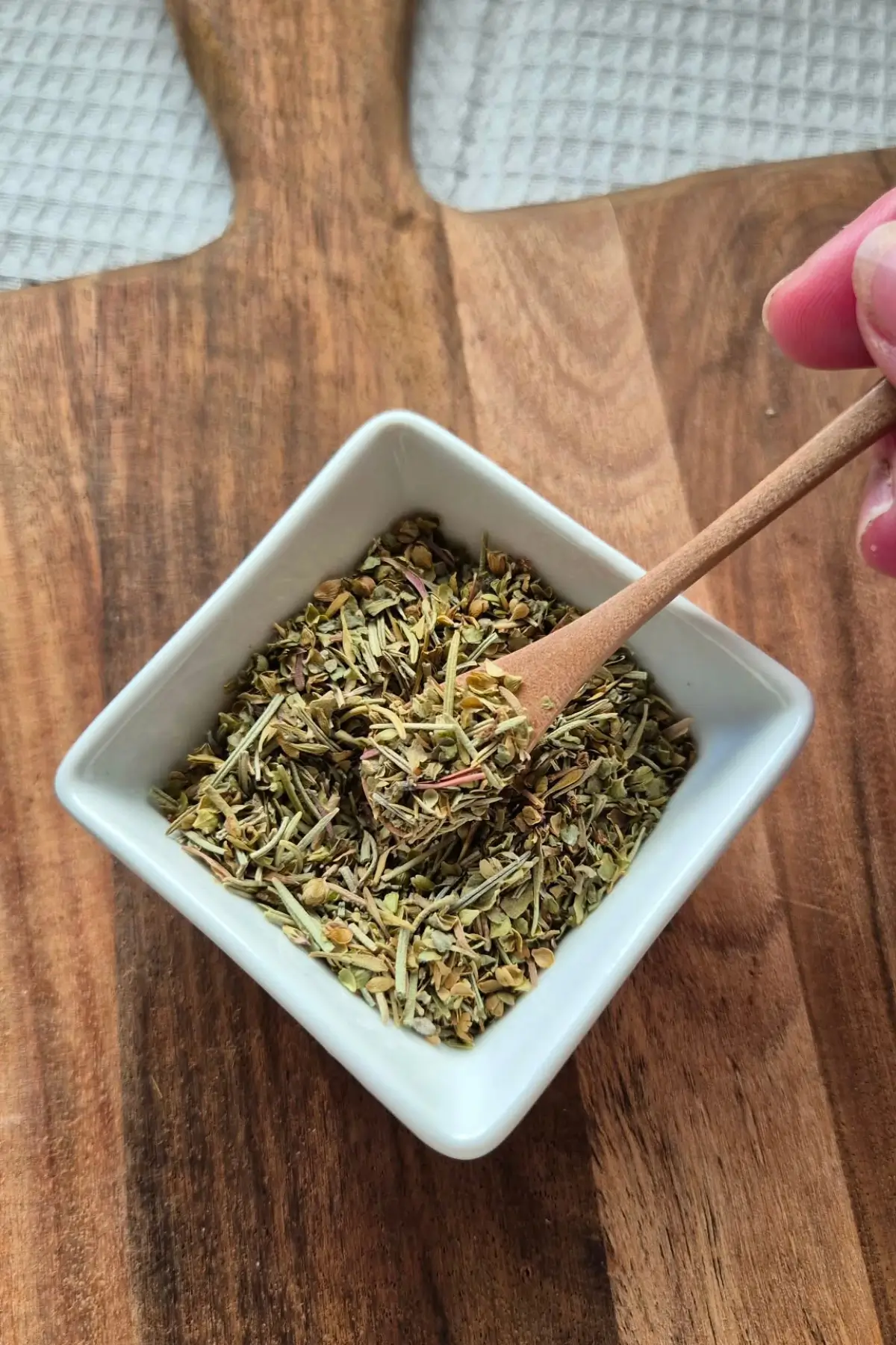 Spoon lifting a portion of the mixed dried herbs from a white bowl.