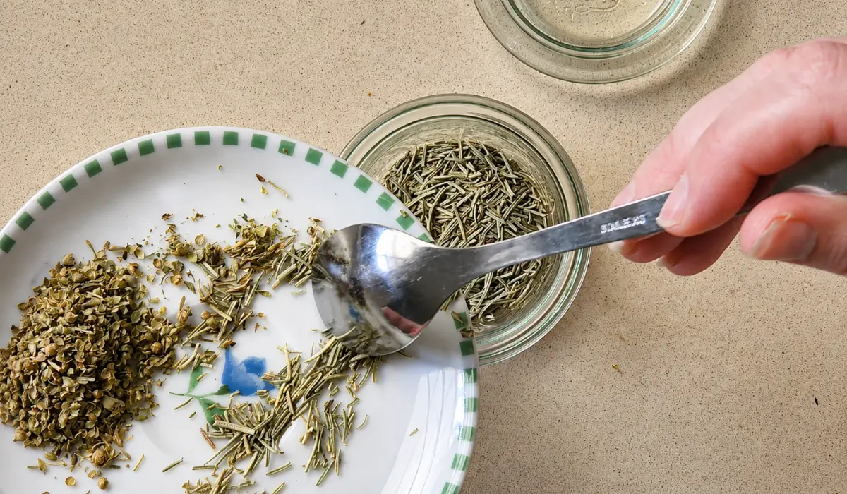 Hand holding a wooden spoon above a bowl filled with mixed dried herbs.