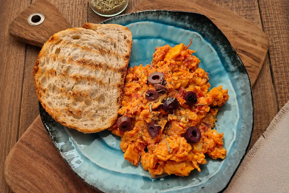 Scrambled Eggs with Tomato served with sliced black olives, Herbes de Provence, and toasted sourdough bread.