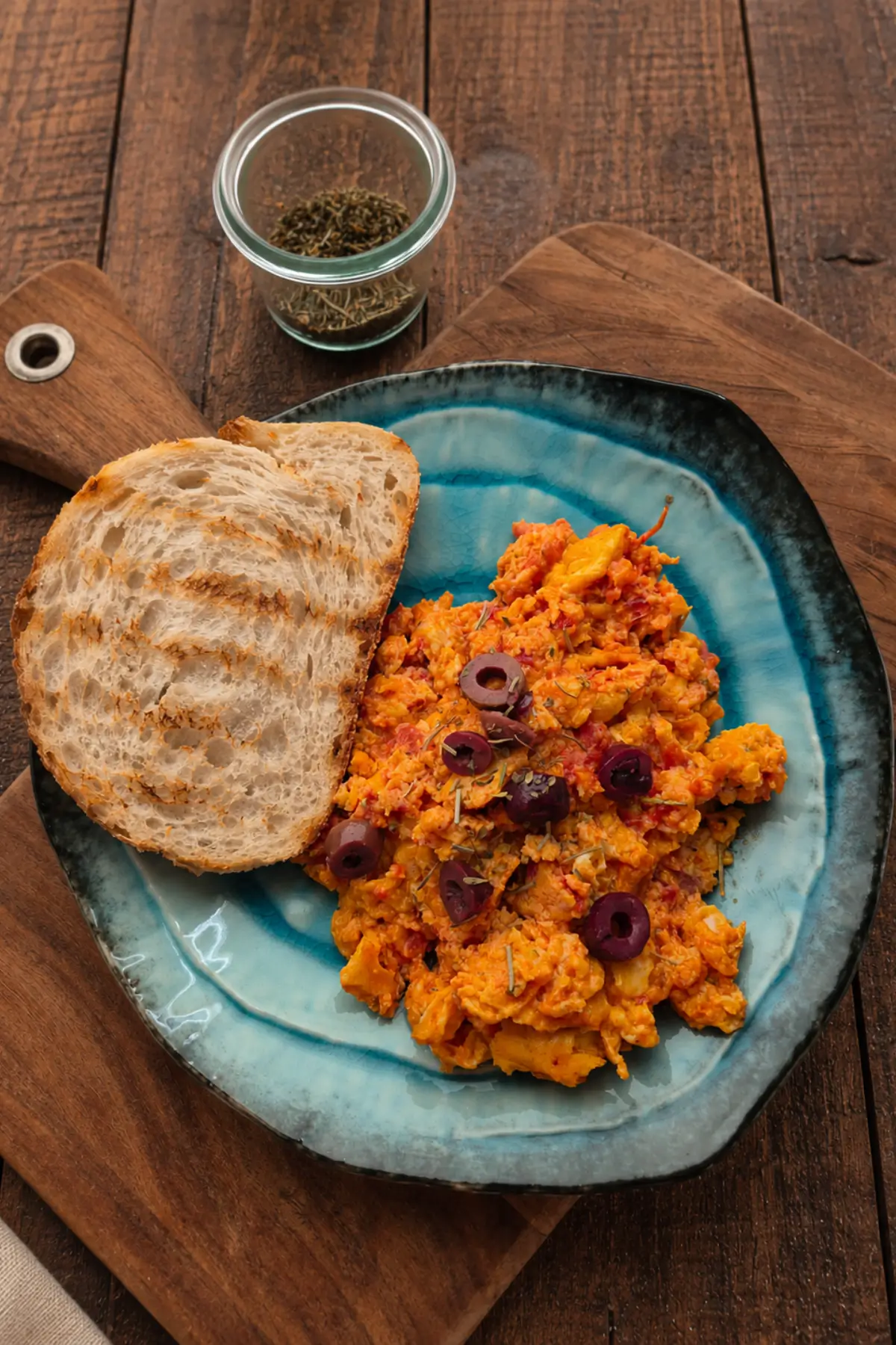 Toast topped with scrambled eggs in tomato sauce, black olives, and herbs.