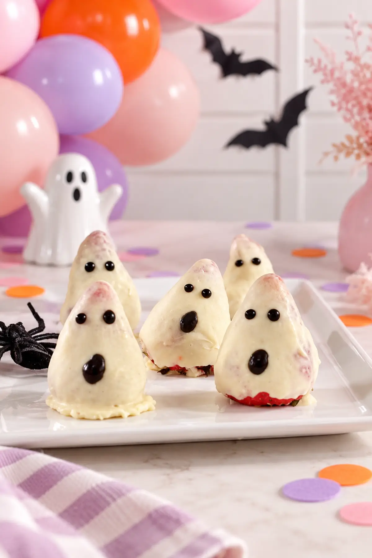 Close-up of white chocolate-coated strawberry ghosts with glossy black eyes and mouths, patches of red strawberry and chocolate pooled around their bases.