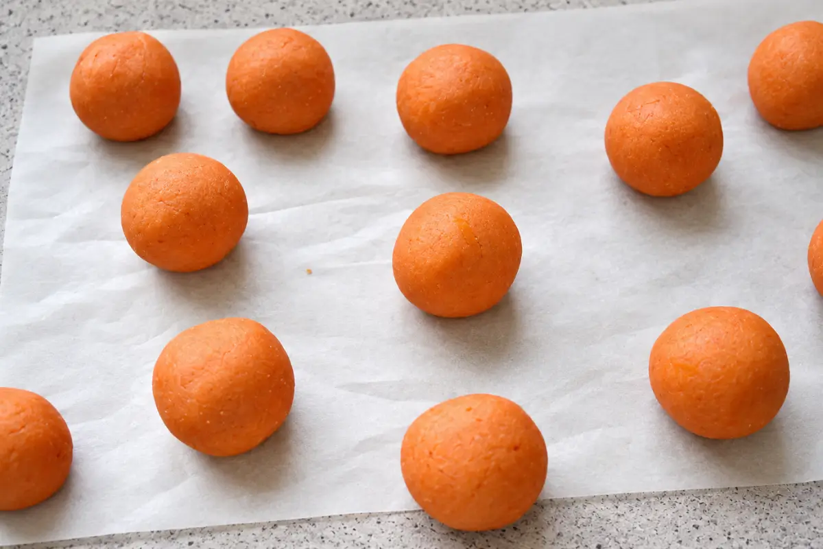 Close view of pumpkin-shaped sweets with dark clove stems and icing faces arranged on a black plate.